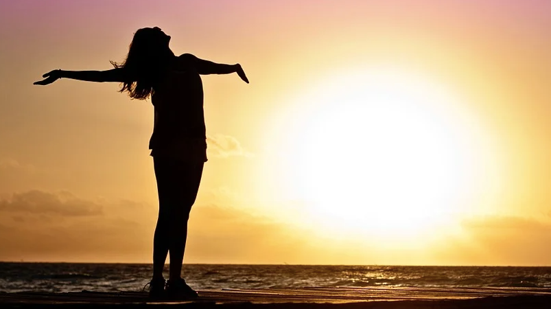 Woman watching sunset with arms thrown back