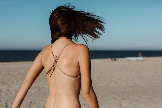 Back view of woman on beach in bikini for 'The best collagen supplements to get summer-ready'